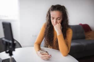 Young sad woman with smart phone in her hand surviving toxic femininity on the internet